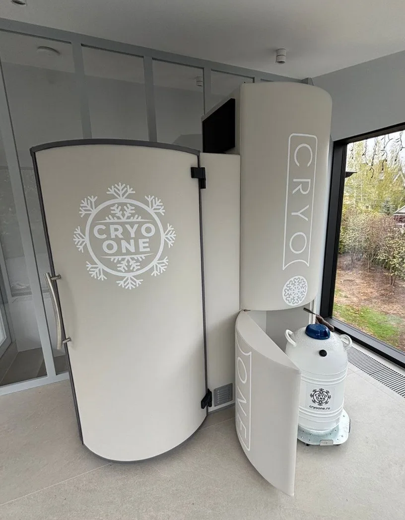 Криокапсула CryoOne Pro: кремово-белая кабина, блок агрегата и сосуд Дьюара в светлом зале с панорамным окном